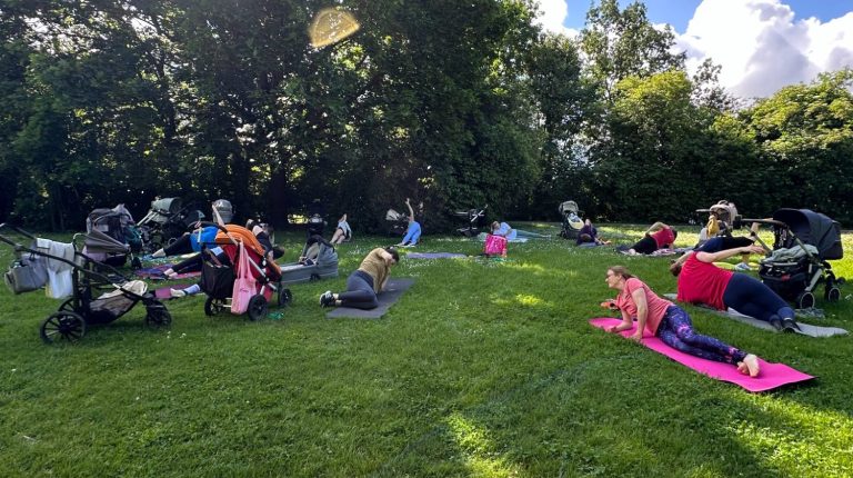 Outdoor Fit mit Baby Frankfurt Mama Fitness Kurs im Sinaipark Frankfurt am Main mit Müttern die auf Sportmatten trainieren. Einige Babys liegen im Kinderwagen.